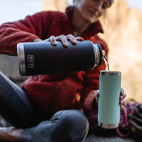 Man pouring from a black YETI Rambler 46 oz bottle into a cup outdoors