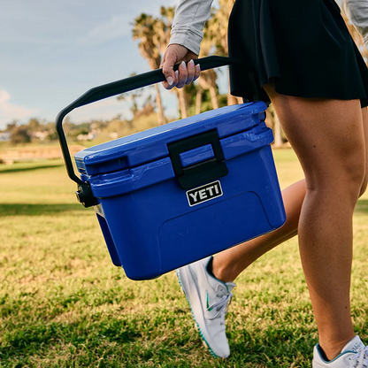 Woman carrying a blue YETI Roadie cool box across a grassy field